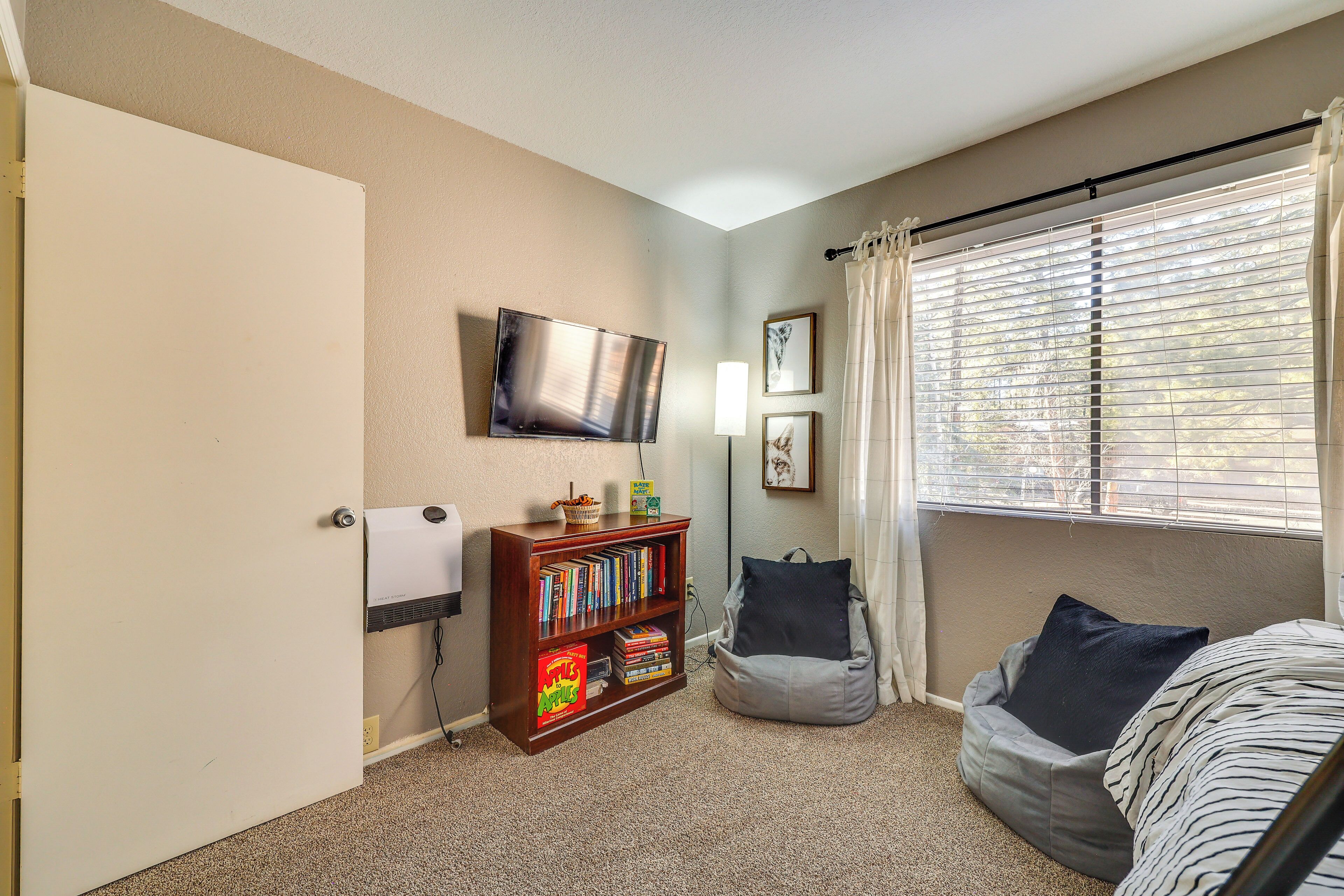 A cozy room with a bookshelf, a bean bag chair, a TV, and a window with blinds.