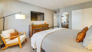 A bedroom with a bed, a chair, a dresser, a mirror, and a floor lamp.