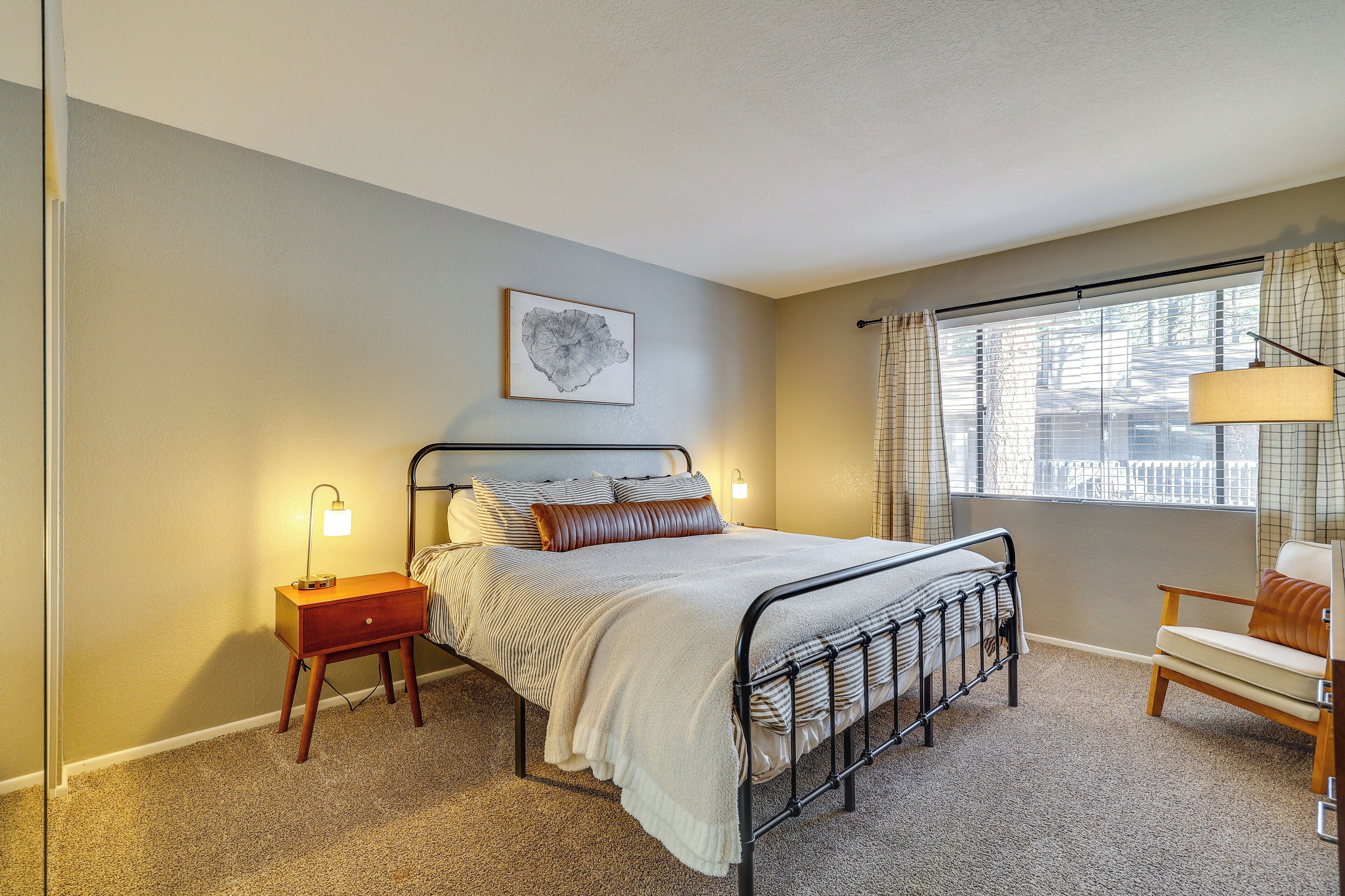 A bedroom with a bed, bedside tables, a chair, a window with curtains, and a wall-mounted lamp.
