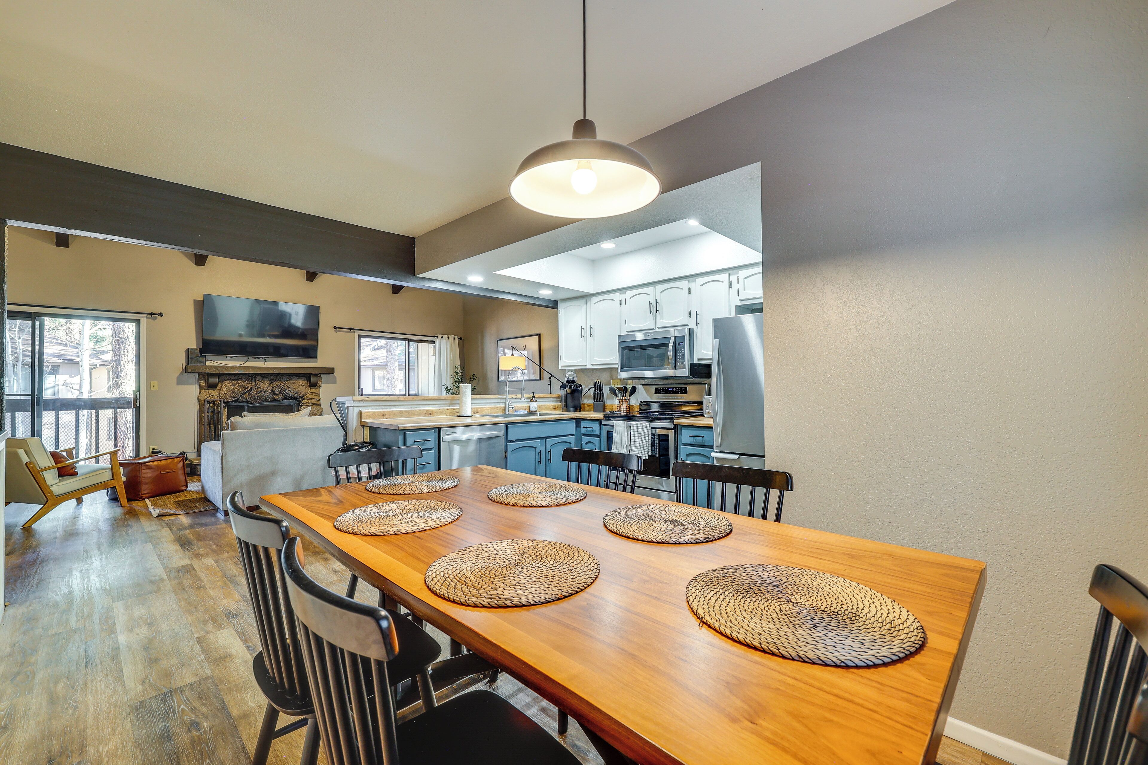 A modern kitchen with a wooden dining table, four chairs, and a hanging light fixture.