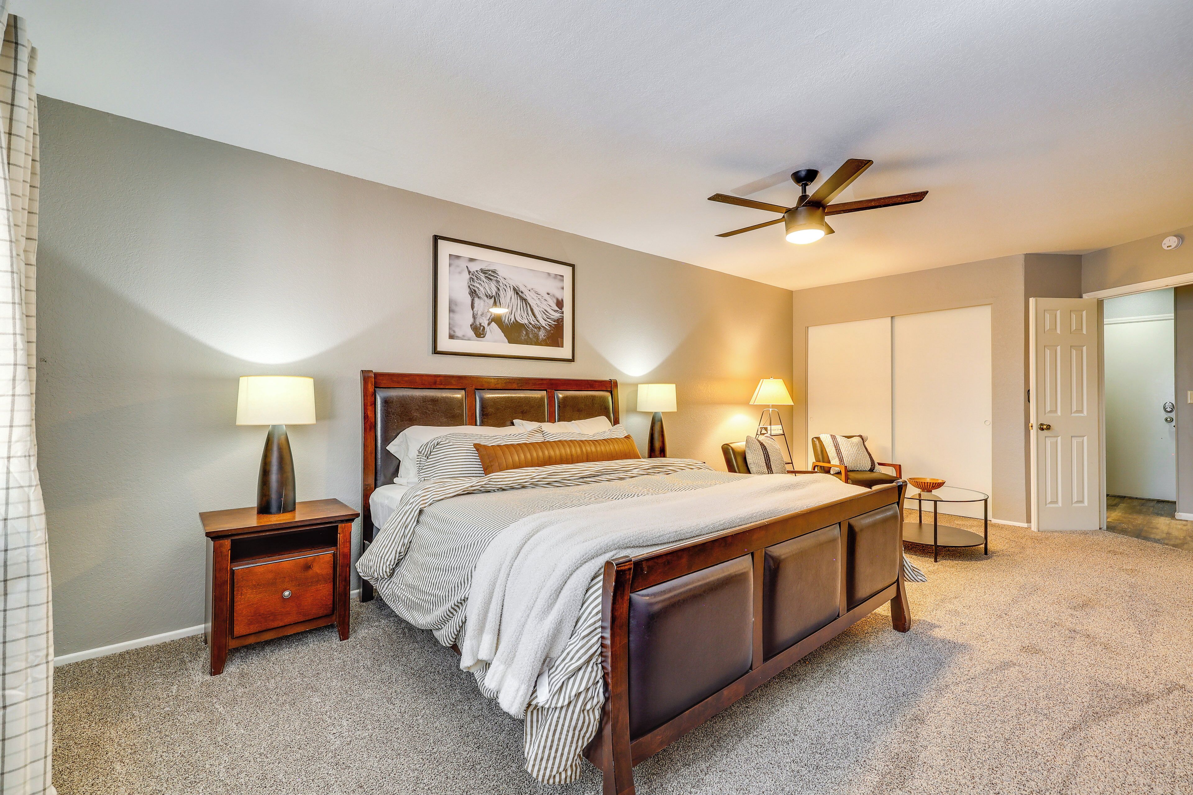 A bedroom with a large bed, two bedside tables, a ceiling fan, and a framed picture on the wall.