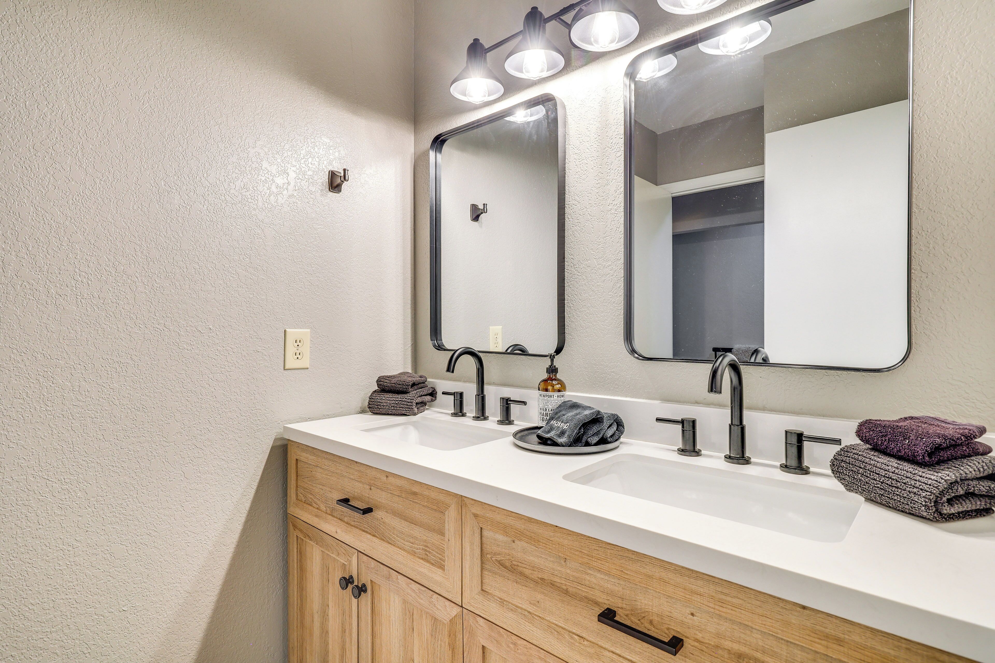 A bathroom with a white sink, two mirrors, and wooden cabinets.