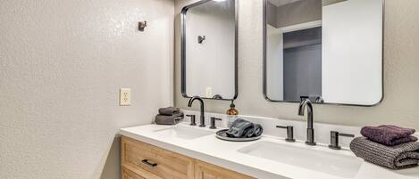 A bathroom with a white sink, two mirrors, and wooden cabinets.
