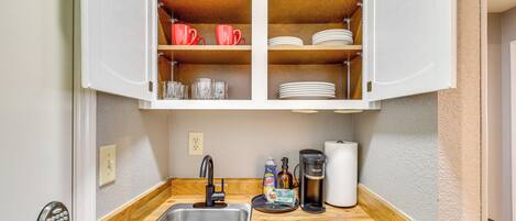 A compact kitchen with a built-in sink, wooden countertop, and open cabinets containing dishes, glasses, and a toaster.