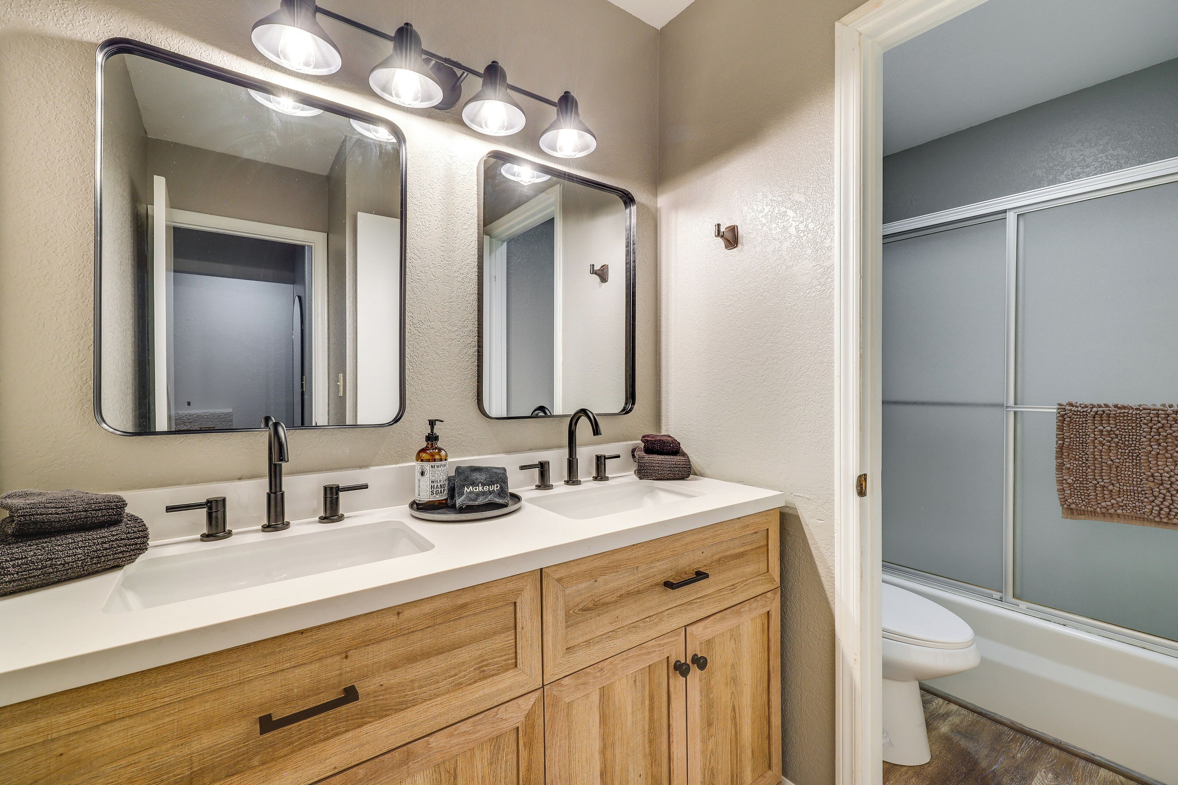 A bathroom with a white sink, two mirrors, a vanity with wooden cabinets, a towel rack, and a shower area.