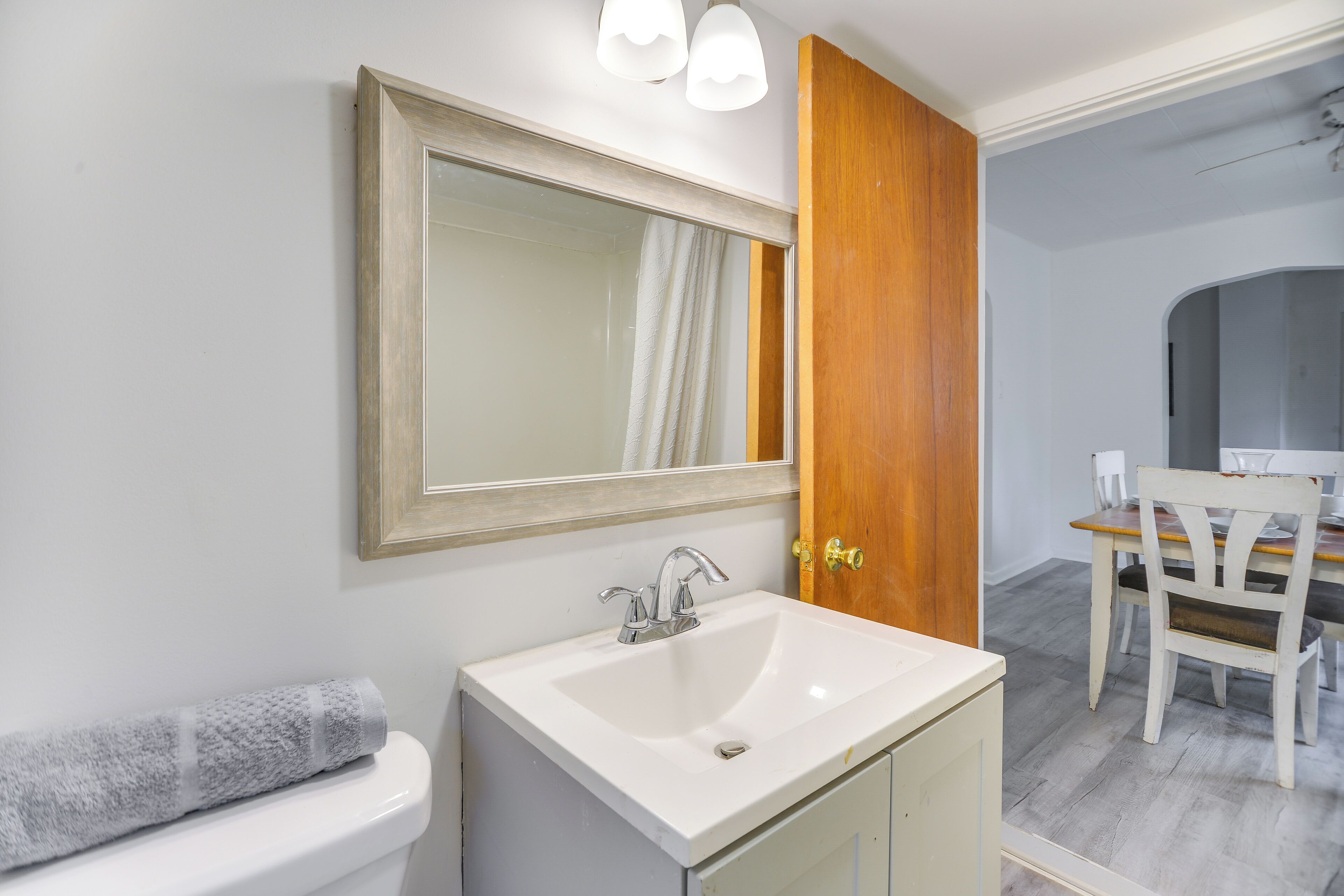 A bathroom with a white sink, a mirror, and a towel on the toilet.