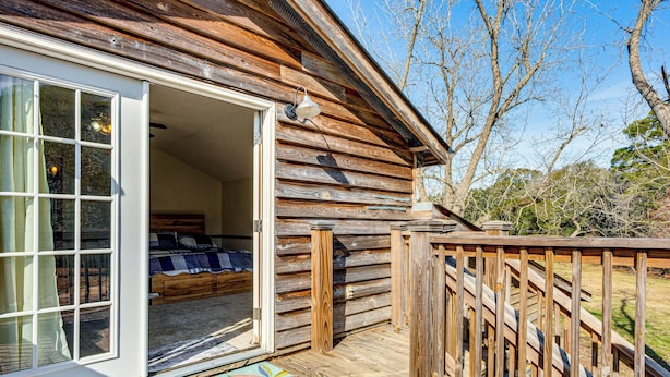 A wooden cabin with a sliding glass door leading to a bedroom with a bed and a window. - Cozy Barn Apt w/ 5-acre Pond in South Georgia! (Doerun)