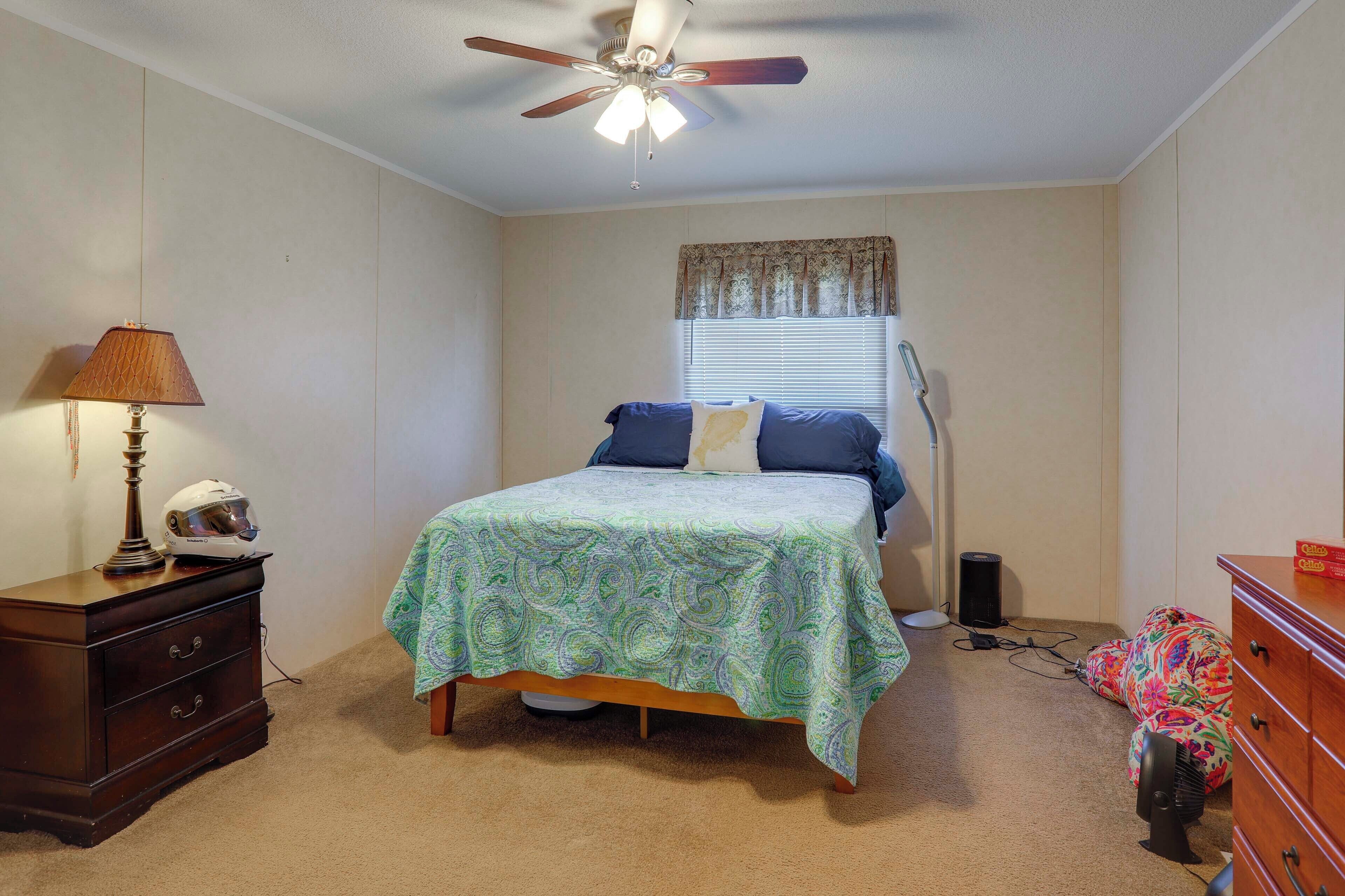 A bedroom with a bed, dresser, nightstand, lamp, ceiling fan, and a window with blinds.