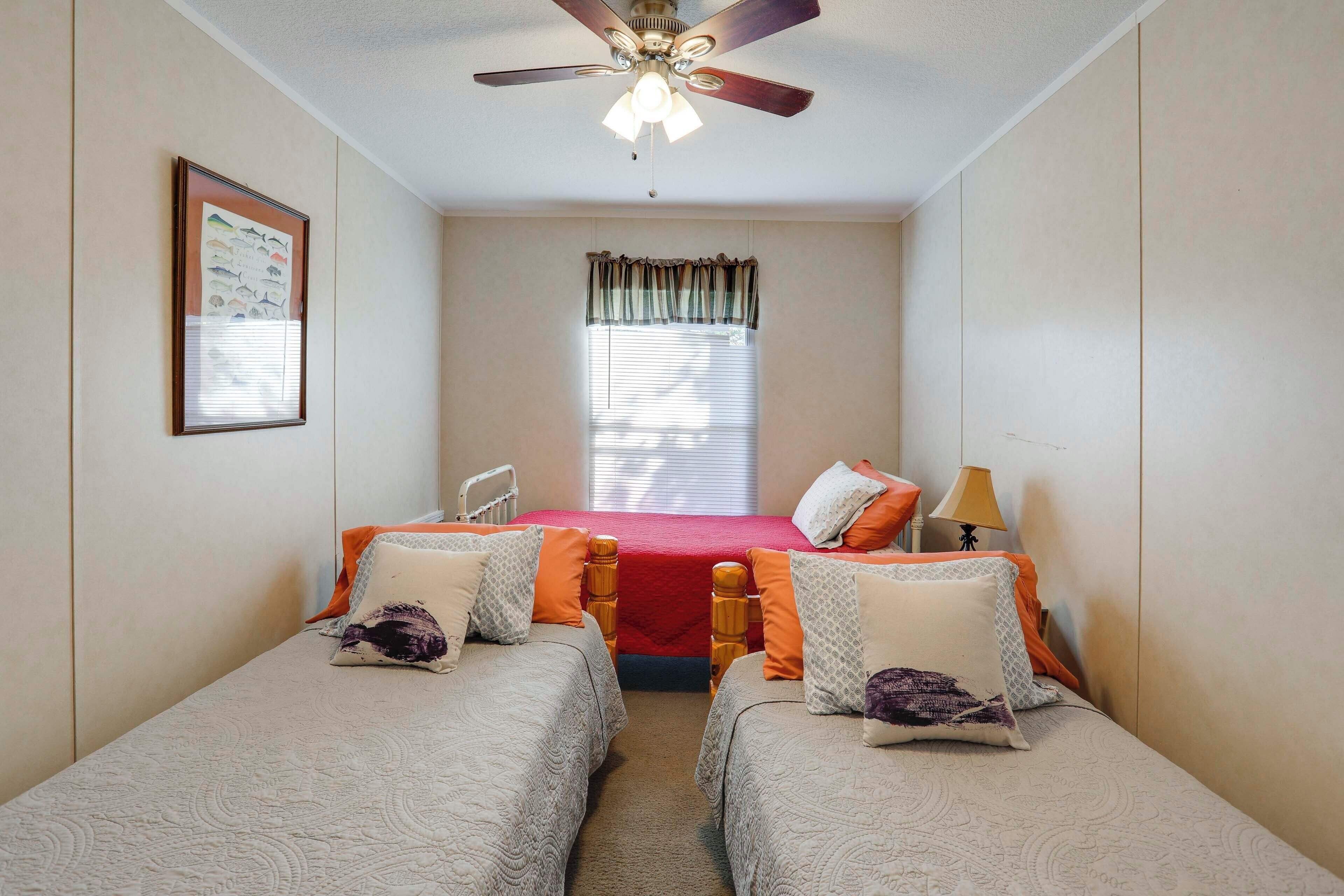 A bedroom with two single beds, a ceiling fan, a window with blinds, and a framed picture on the wall.