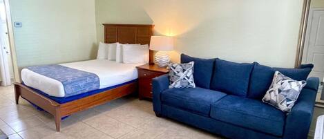 A bedroom with a bed, a blue sofa, a nightstand, and a ceiling fan.