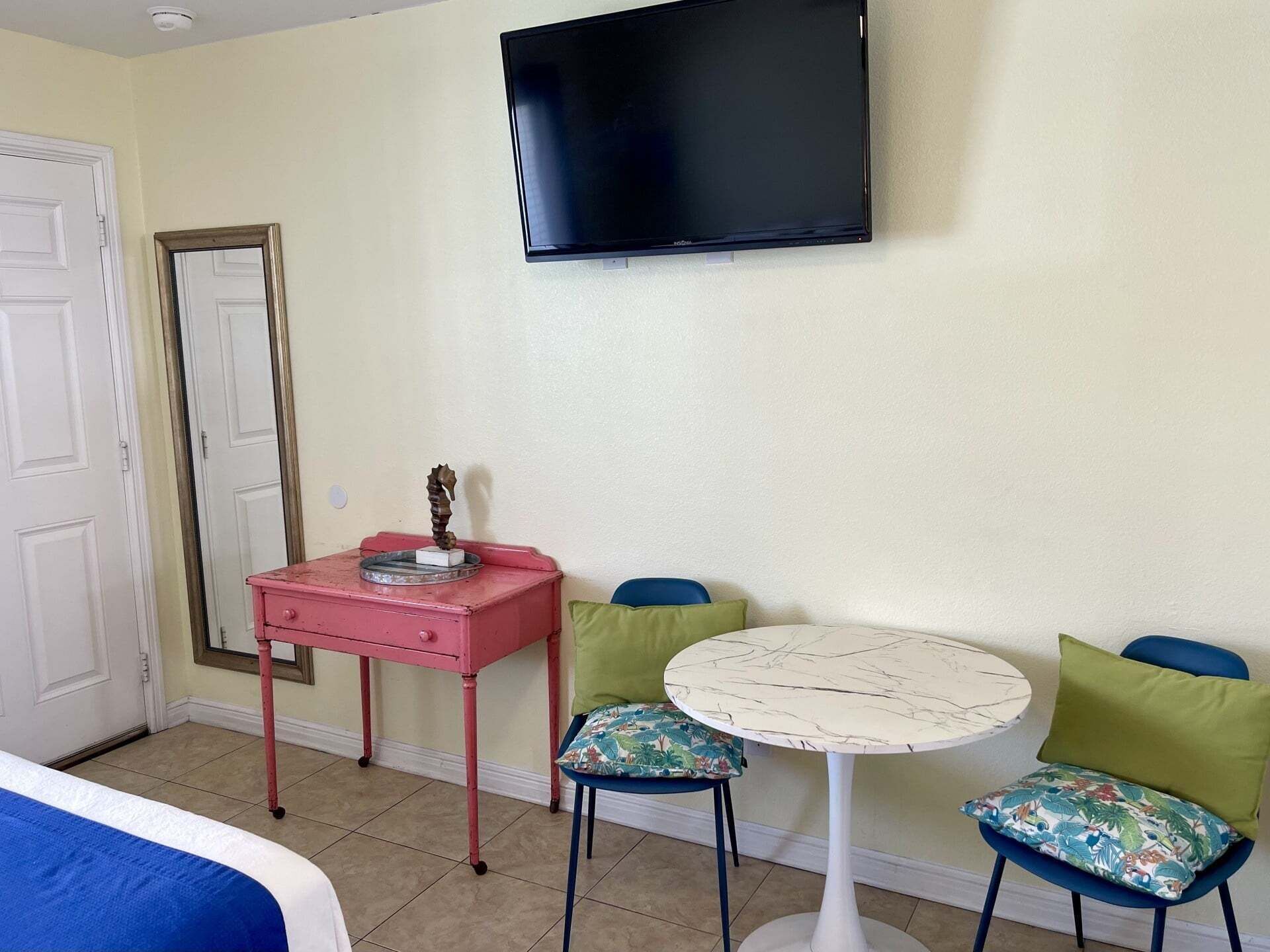 Una habitación de hotel con una cama, un tocador rosa, un televisor y dos sillones con cojines.