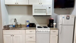 Eine kompakte Küche mit weißen Schränken, einer Mikrowelle, einem Herd, einem Kühlschrank, einer Spüle und einer Kaffeemaschine.