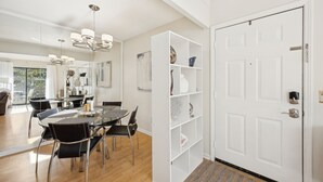 A modern dining area with a glass table and chairs, a white shelving unit with decorative items, and a white door with a doorknob. - Forest Ridge U8 2 Bedroom Condo (Fernandina Beach)