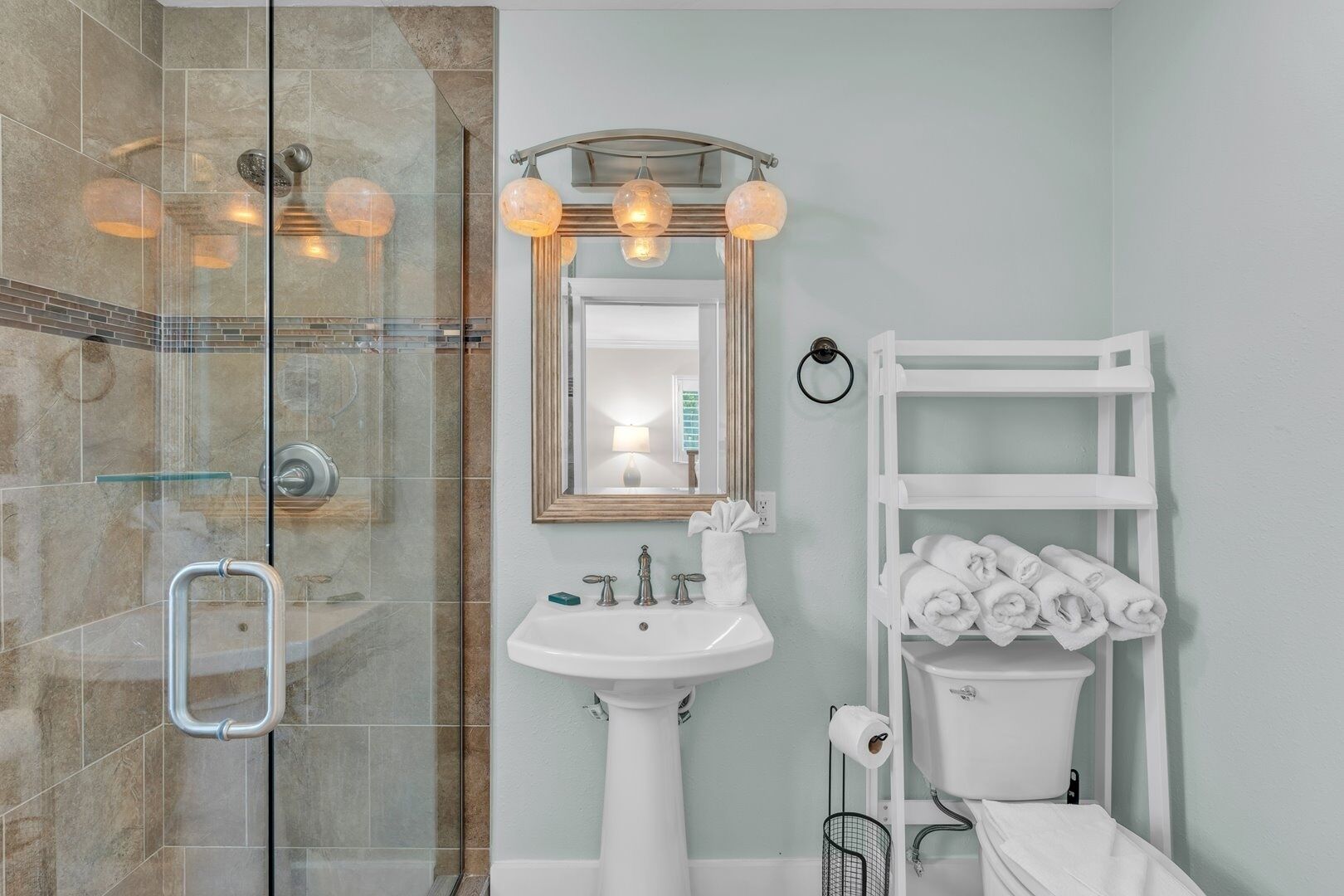 Un baño con cabina de ducha de vidrio, un lavabo blanco, un espejo y un perchero para toallas.