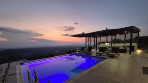 Ein Infinity-Pool auf dem Dach mit Blick auf den Horizont, eine überdachte Sitzgelegenheit im Freien und ein Grill.