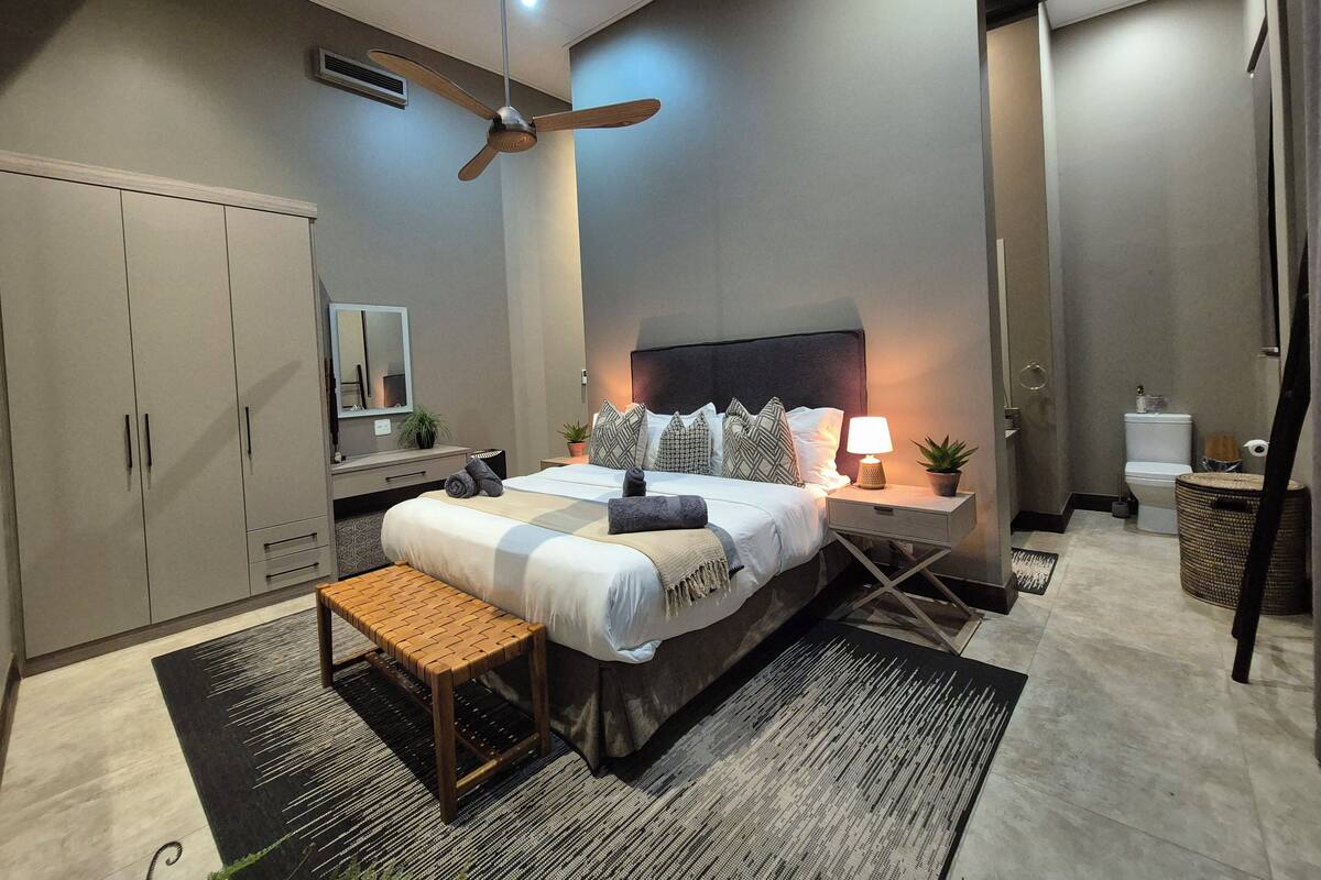 Une chambre à coucher moderne avec un lit, une table de chevet, une commode et un ventilateur de plafond.