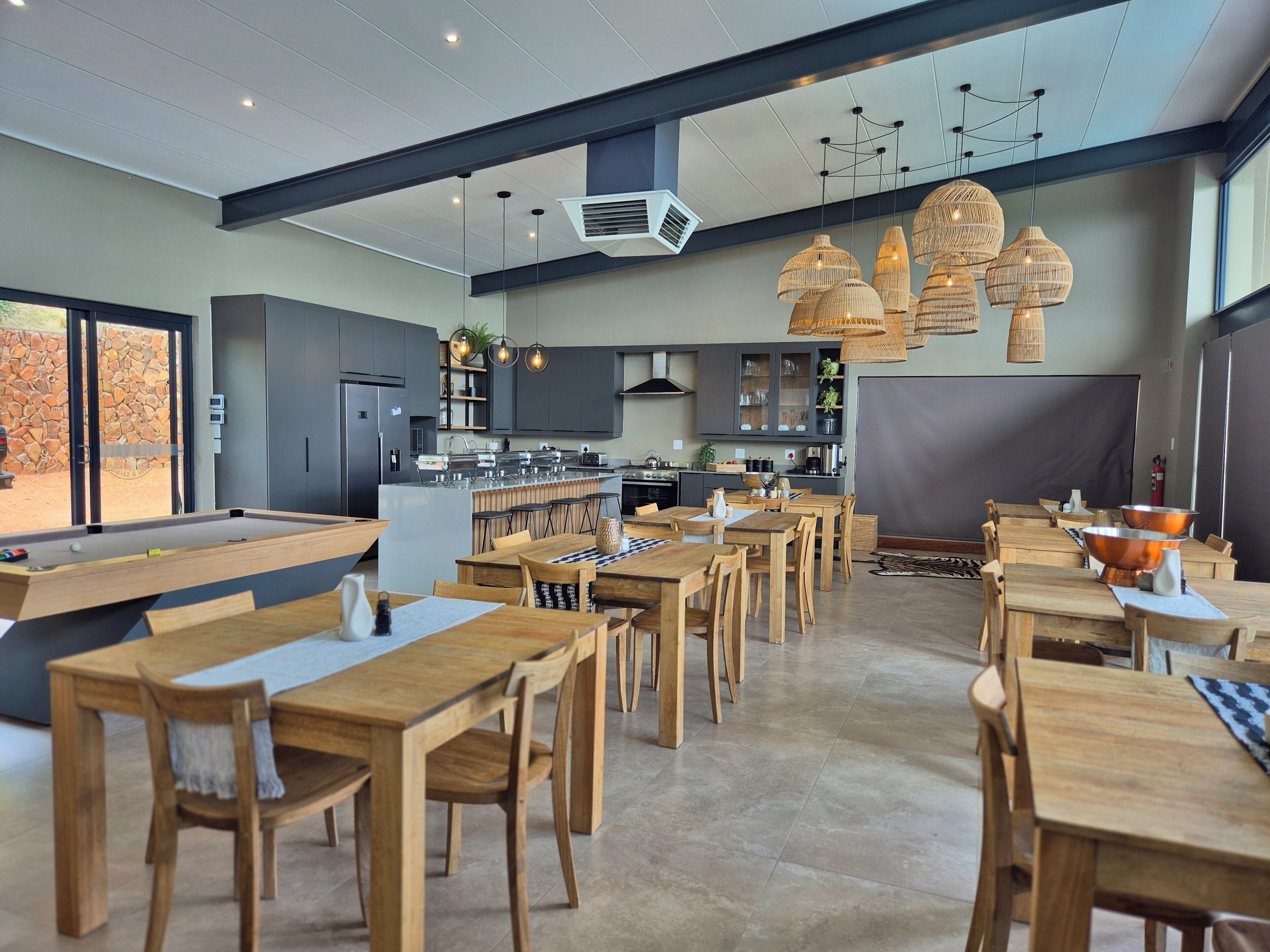 A modern dining area with wooden tables and chairs, a pool table, and a kitchen in the background.