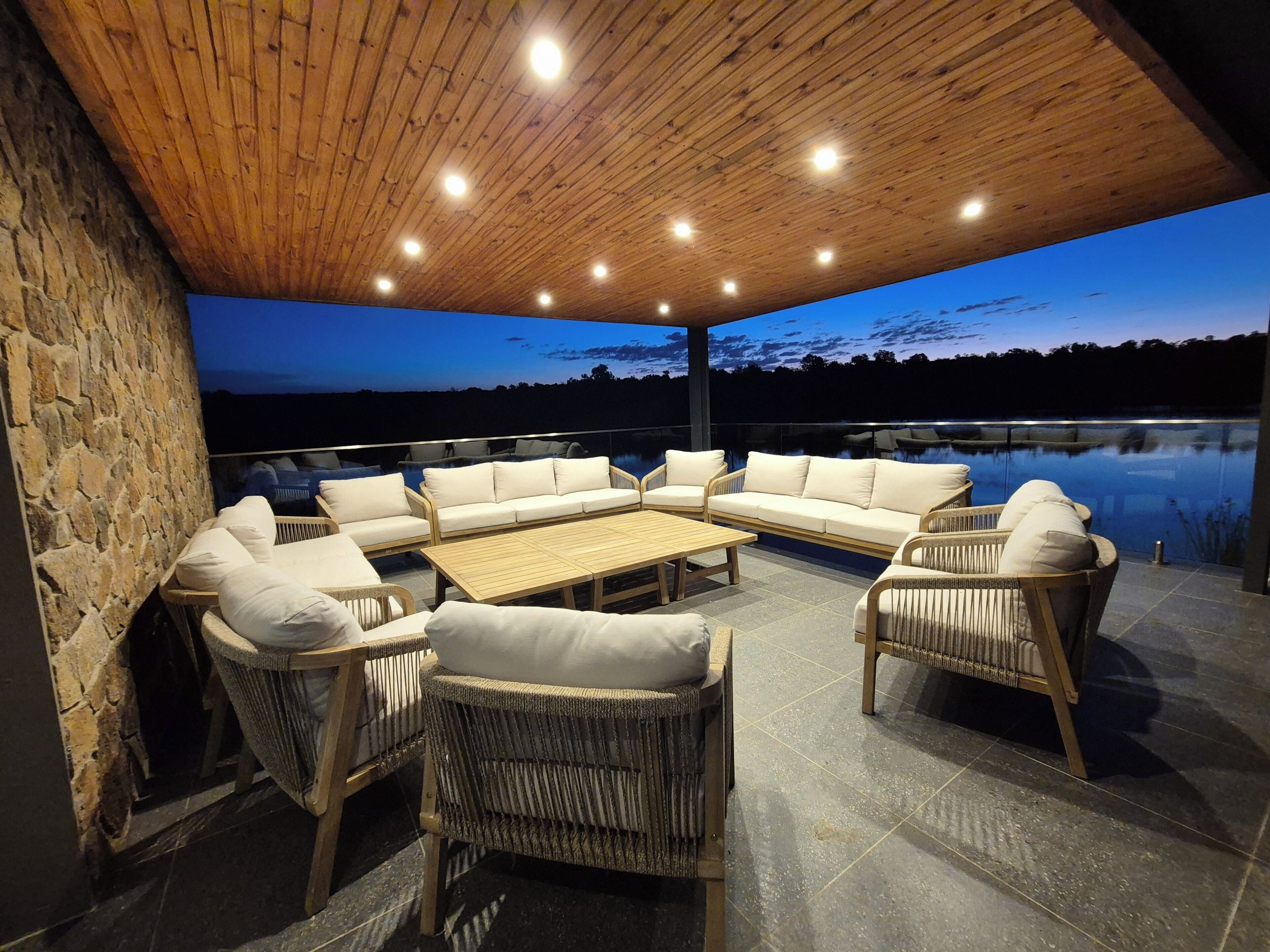 An outdoor patio area with wicker furniture and a stone wall, overlooking a body of water.