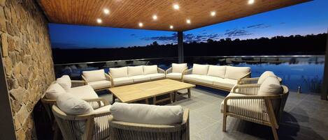 An outdoor patio area with wicker furniture and a stone wall, overlooking a body of water.