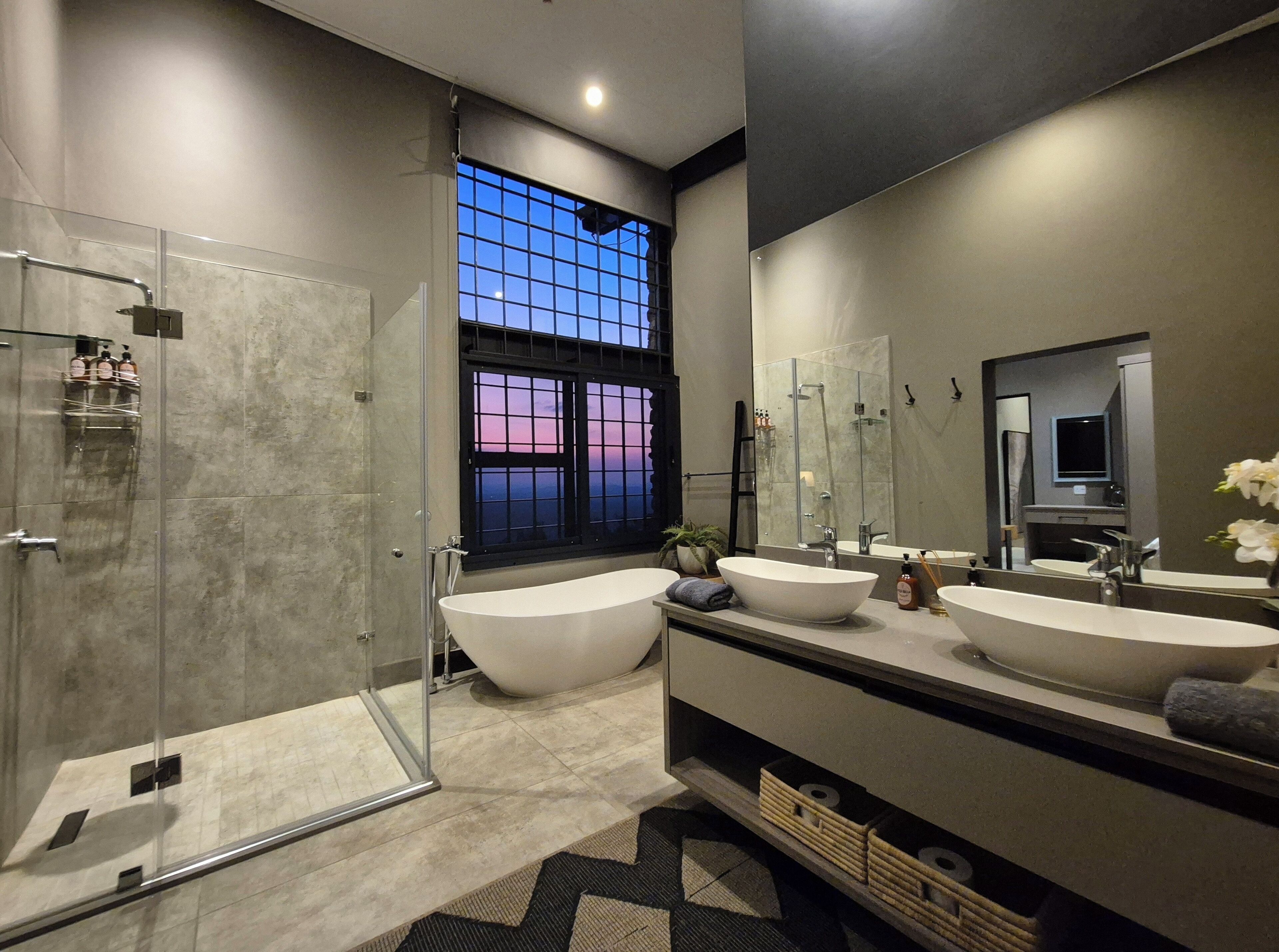 Un baño moderno con cabina de ducha de vidrio, un ventanal con vistas y dos lavabos con espejos.