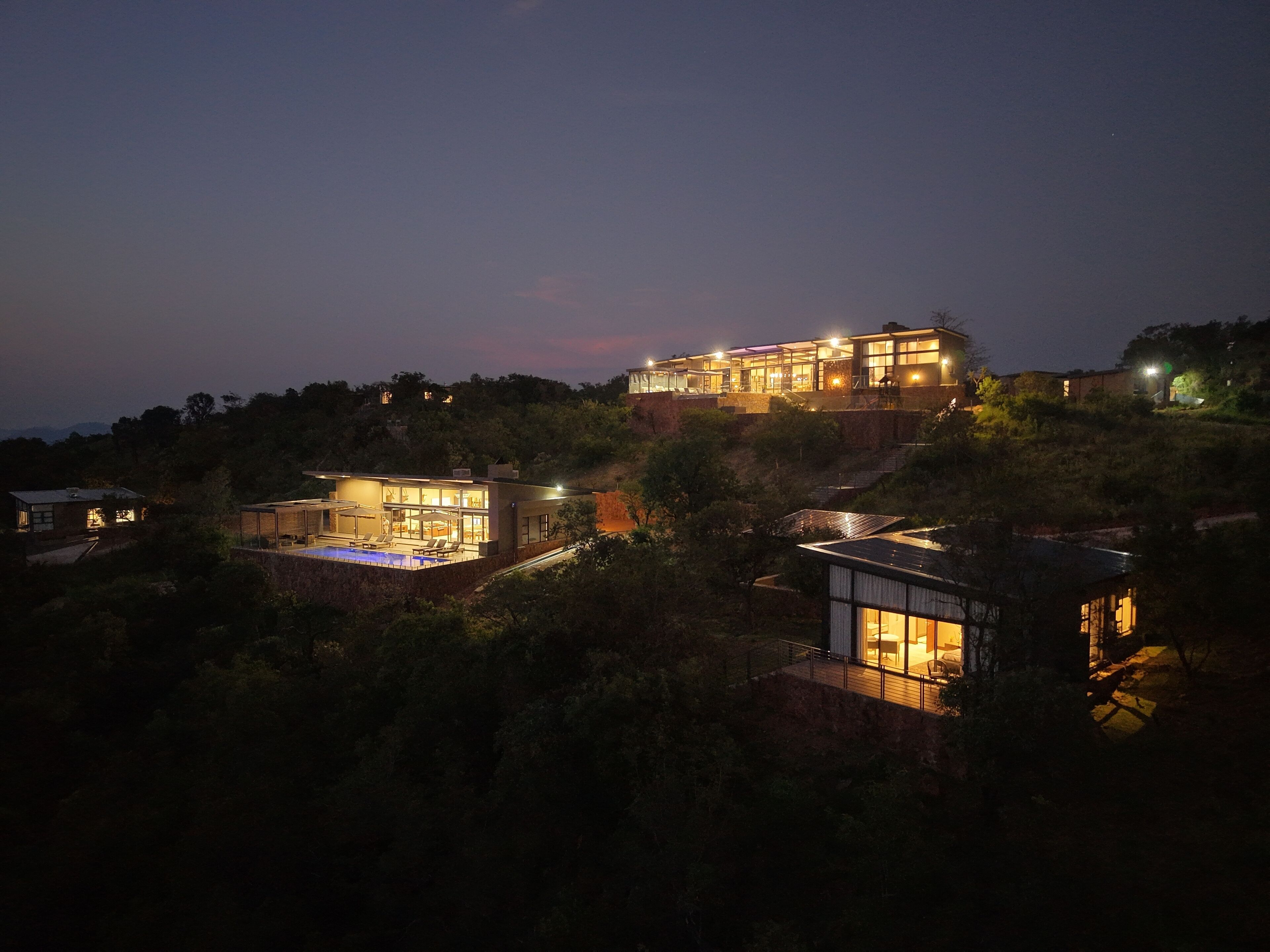 A modern hillside property with multiple buildings, including a main house with large windows and a swimming pool.