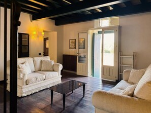 A living room with a white sofa, a glass coffee table, and a wooden floor. There is a door leading to a balcony.