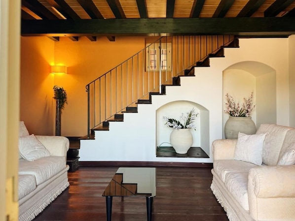 A living room with a staircase, two sofas, a coffee table, and decorative vases.