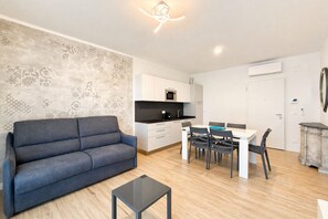 Ein modernes Wohnzimmer mit einer Couch, einem Esstisch mit Stühlen, einer Küchenzeile inklusive Schränken und Geräten sowie einer Wand mit Dekoration.