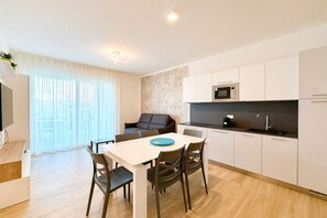 Eine moderne Küche mit weißen Schränken, einer Mikrowelle und einem Spülbecken. Im Wohnbereich befindet sich ein Esstisch mit Stühlen sowie eine Couch.