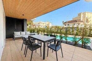 Eine Terrasse mit Tisch, Stühlen und einer Sitzecke, Blick auf einen Swimmingpool und Gebäude.