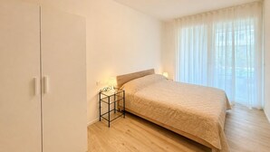 A bedroom with a bed, bedside lamps, a wardrobe, and a window with curtains. - Aurora Sand 2 - Carraro immobiliare Jesolo (Lido di Jesolo)