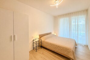 Ein Schlafzimmer mit einem Bett, Nachttischlampen, einem Kleiderschrank und einem Fenster mit Vorhängen.