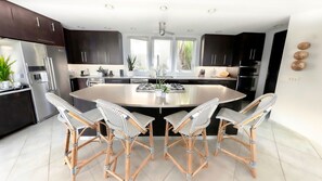 A modern kitchen with dark cabinets, a stainless steel refrigerator, a central island with a sink, and four wicker chairs around a round table. - La Bella Sorella breathtaking panoramic views on island! (St. John)