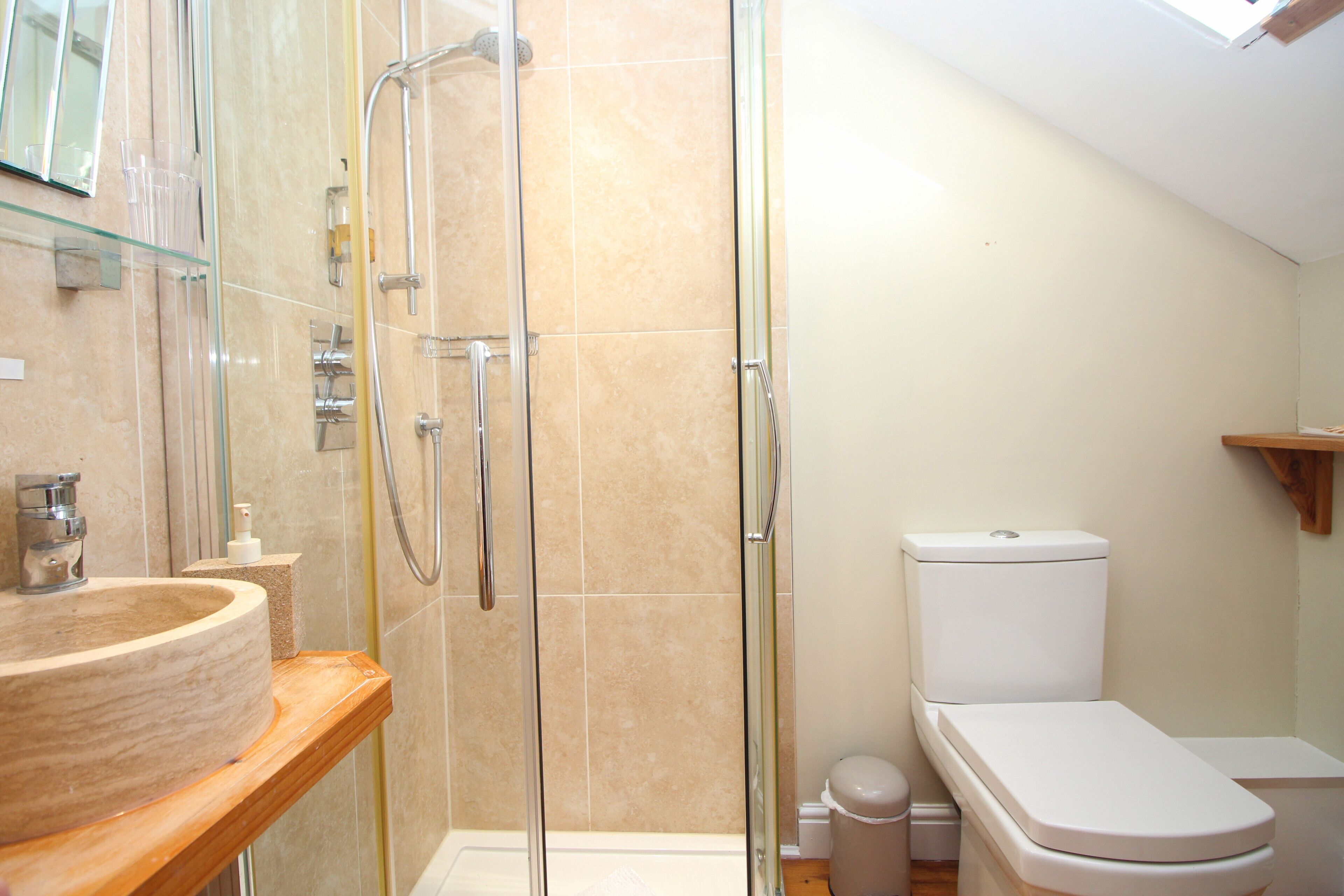 A bathroom with a glass shower enclosure, a wooden vanity with a beige sink, and a white toilet.