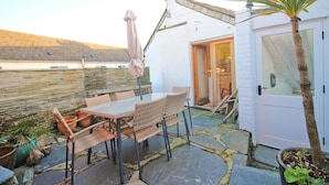 A patio with a table and chairs, a white door, and a stone wall. - Unique town house with games room (Padstow)