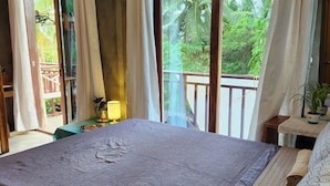 A bedroom with a large bed, a balcony with a view of greenery, and a ceiling fan. - Balay Yuhom (General Luna)