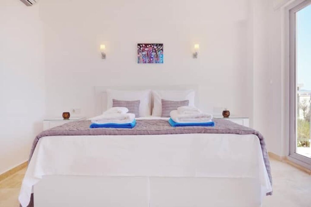 A spacious bedroom with a large bed, two bedside tables, and a view through a large window.