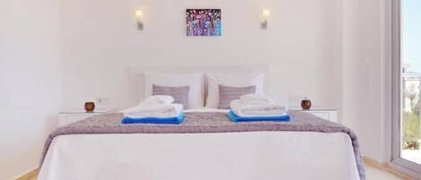 A spacious bedroom with a large bed, two bedside tables, and a view through a large window.