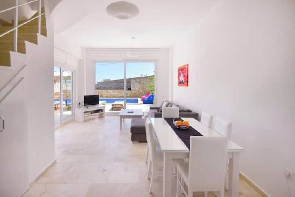 Un espace de vie moderne comprenant une table à manger, des meubles blancs et une grande fenêtre donnant sur l’extérieur.