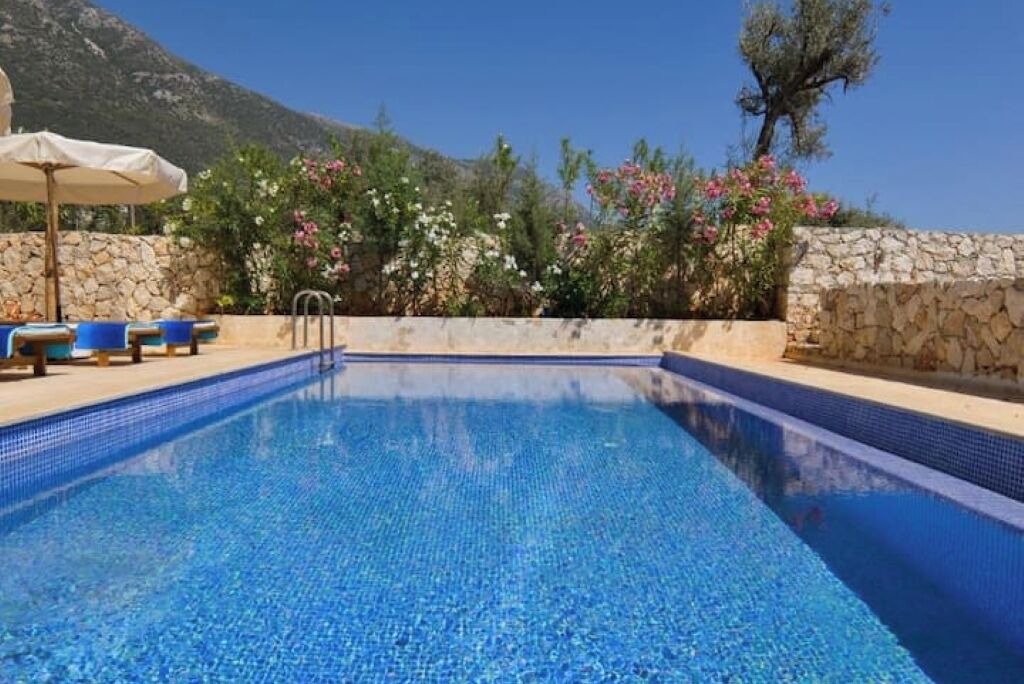 Una piscina azul cristalina con un muro de piedra y sillones de descanso.