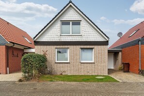 A two-story house with a brick facade, two windows with shutters, a satellite dish, and a small lawn. - Holiday home 'Me(e)rzeit' in Schillig (Schillig)