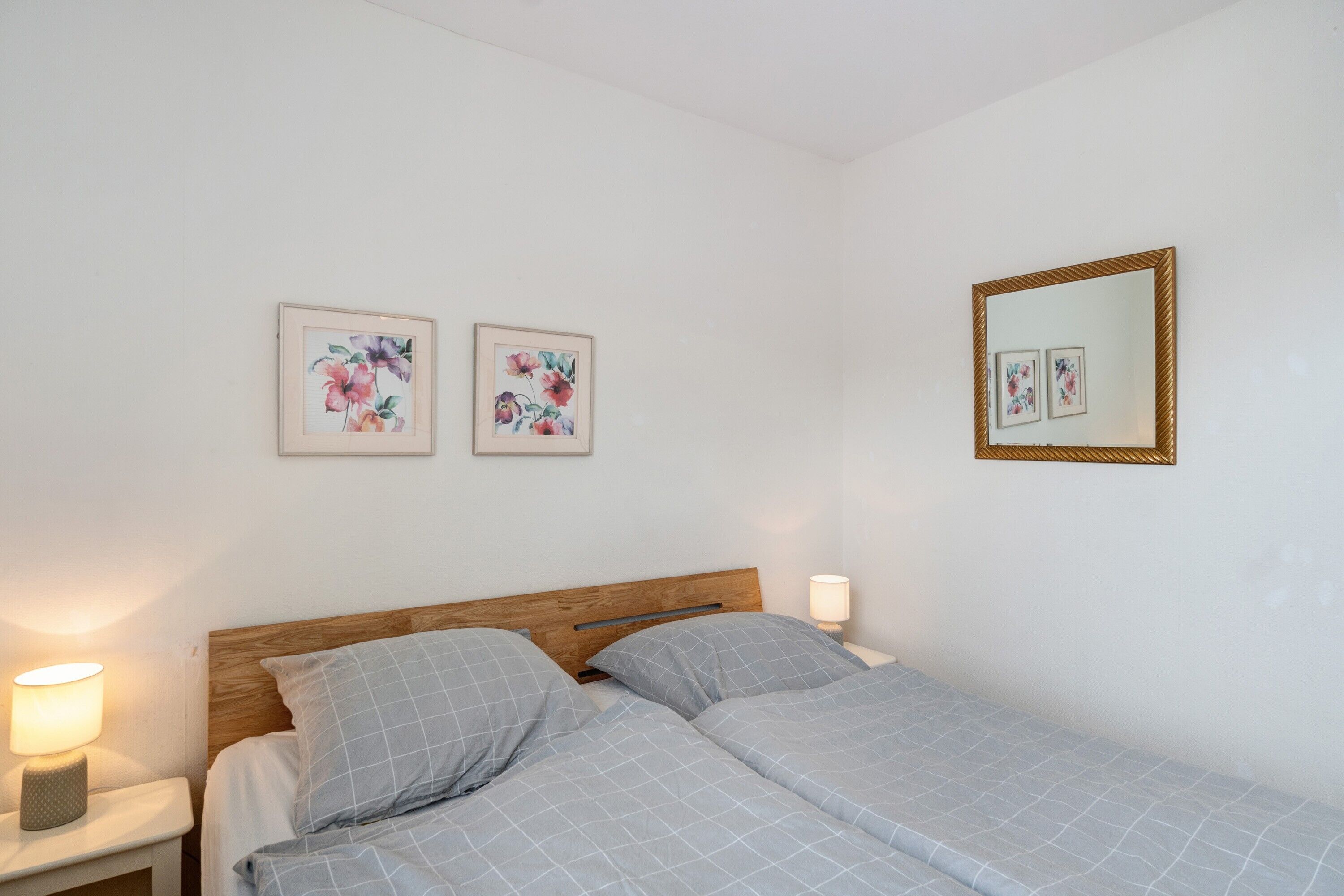 Una cama doble con cabecera de madera, dos lámparas de noche y dos cuadros con motivos florales en la pared.