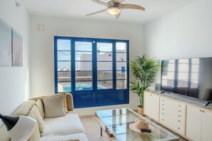 Ein modernes Wohnzimmer mit einer Couch, einem Glastisch, einem Fernseher und einem großen Fenster mit Blick auf einen Swimmingpool.
