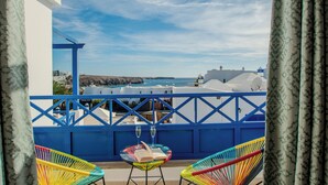 A balcony with two colorful chairs, a table with a book and a glass, and a view of the sea and buildings. - Villa Vereda Del Sur - Sea View, Pool, close to promenade, shops and supermarket (Playa Blanca)