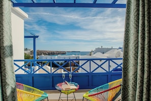 Ein Balkon mit zwei bunten Stühlen, einem Tisch mit einem Buch und einem Glas, und Blick auf das Meer und die Gebäude.