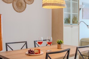 Ein Esstisch mit zwei Weingläsern, einer Traubentafel und Käse. An den Wänden sind Flechtpaneele angebracht, und über dem Tisch hängt eine Leuchte.