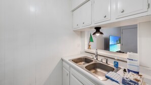 Cucina con mobili bianchi, un lavello doppio e un piano di lavoro con una spugna e un dispenser per il sapone.