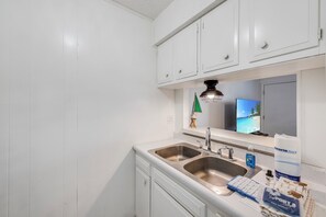 A kitchen with white cabinets, a double sink, and a countertop with a dish sponge and soap dispenser. - This is the perfect cozy island bungalow for a weekend of fishing or just hangin (Port Aransas)