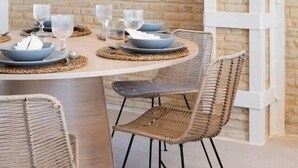 Ett runt matbord med fyra flätade stolar, dukat med tallrikar, skålar och glas, placerat framför en tegelvägg med en vit, rutmönstrad struktur.