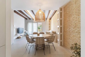 Uma área de refeições com uma mesa redonda, cadeiras de vime e um lustre.